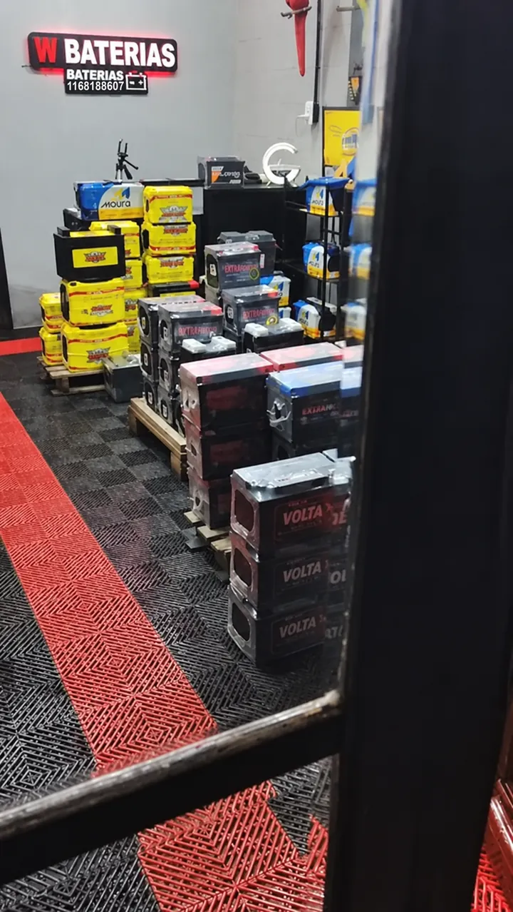 Cartel de W.Baterías en el local, con baterías nuevas apiladas sobre el piso rojo y negro